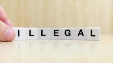 Üzerinde harfler yazan beyaz kiremitleri kullanarak yasadışı sözcüğü yasaya dönüştüren bir el.