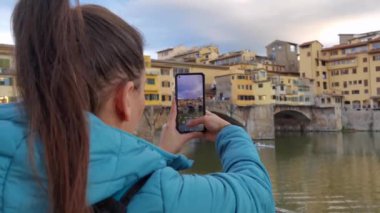 Floransa 'yı ziyaret eden ve ünlü Ponte Vecchio' da akıllı telefonuyla fotoğraf çeken bir turist kız.