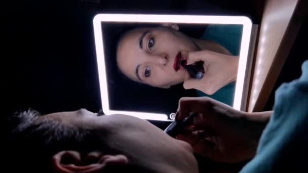 彼女は彼女の唇に赤い口紅を置いている鏡の前に少女の顔のクローズアップ — ストック動画