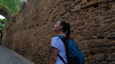 Güneşli bir günde tarihi şehir merkezinde eski bir duvarın yanında bir kız yürür.