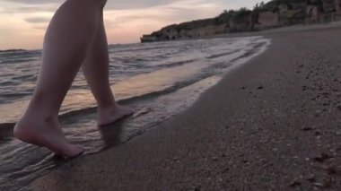 Gün batımında Anzio sahilinde yürüyen kız deniz dalgaları ayaklarına ulaşırken kumdaki ayak izlerini siliyor.