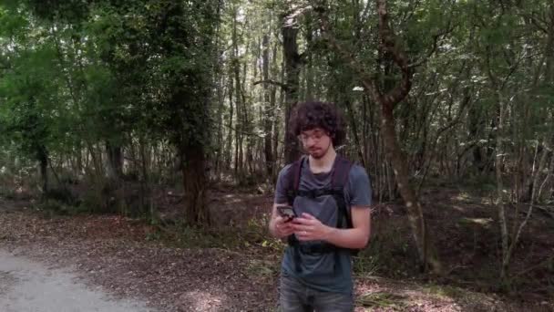 トレッキングバックパックを持っている少年は 彼のスマートフォンを使用してラティナ自然保護区の森で自分自身を浸透させます — ストック動画