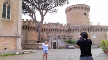 Ostia Antica köyündeki ortaçağ şatosunun önünde bir kızın fotoğrafını çeken bir çocuk.