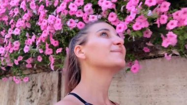 Gülümseyen bir kızın yüzüne yakın çekim Pembe çiçeklerle dolu bir çalılığın önünde yürüyor