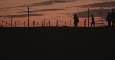 A closeup shot of tourists walking on the side of the Washington Monument. Silhouettes are taken. Clouds are shown with an orange sunset. High quality 4k Footage 