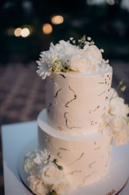 beautiful wedding cake with white roses in the background on a blurred of a restaurant
