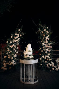 beautiful wedding cake on the background of the evening ceremony area decorated with flowers