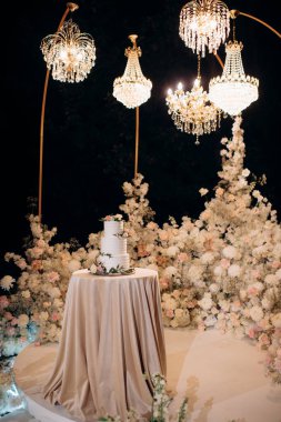 beautiful wedding cake on the background of the evening ceremony area decorated with flowers