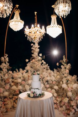 beautiful wedding cake on the background of the evening ceremony area decorated with flowers