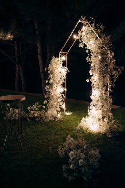 beautiful wedding arch with white flowers and lamps in the garden, night ceremony