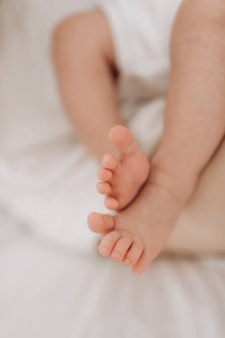 Legs and fingers of a newborn baby lying on a white bed close-up, motherhood, child care, caring parents