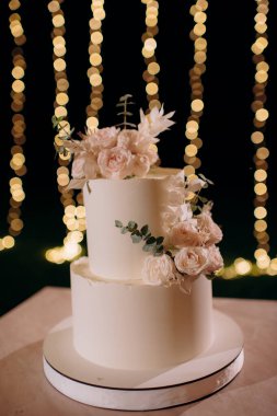 Küçük bir masanın üzerindeki çiçeklerle süslenmiş zarif, iki katlı düğün pastası düğün kemerinin arka planına karşı.