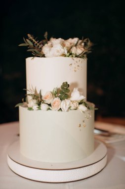 Küçük bir masanın üzerindeki çiçeklerle süslenmiş zarif, iki katlı düğün pastası düğün kemerinin arka planına karşı.