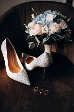 Gelinin kıyafetlerinin ayrıntıları, şık düğün aksesuarlarının modern bir kompozisyonu, yüksek topuklu ayakkabılar, altın alyanslar. Düğün hazırlıkları.