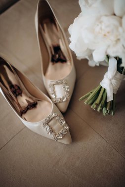 Gelinin kıyafetinin detaylarının yakın plan çekimi şık düğün aksesuarları, yüksek topuklu ayakkabılar, modern bir gelin buketi beyaz şakayık. Düğün hazırlıkları.