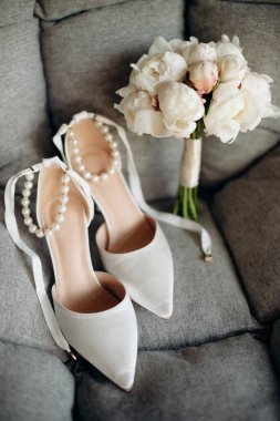 Gelinin kıyafetinin detaylarının yakın plan çekimi şık düğün aksesuarları, yüksek topuklu ayakkabılar, modern bir gelin buketi beyaz şakayık. Düğün hazırlıkları.
