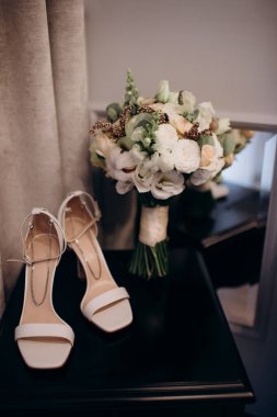 Gelinin kıyafetinin detaylarının yakın plan çekimi modern bir düğün aksesuarı, yüksek topuklu ayakkabılar, modern bir gelin buketi. Düğün hazırlıkları.