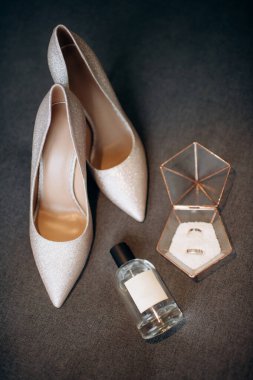 Çekici bir gelin için zarif düğün aksesuarlarının modern bir kompozisyonu. Alyanslar, şık moda ayakkabılar, bir şişe parfüm, siyah arka planda mücevherler.