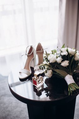 Düğün aksesuarı gelin. Küpeler, şık bir düğün buketi, siyah masadaki parfüm. Yakın çekim..
