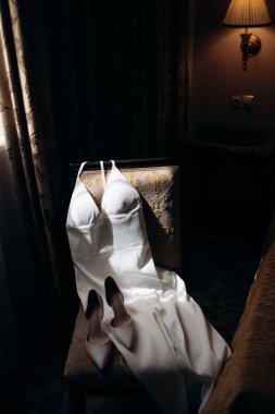 Modern bir gelinlik yumuşak sabah ışığında şık bir sandalyede yatar. Işıkta parıldayan şık bir gelinlik..