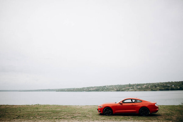 красный спортивный автомобиль на фоне озера и красивого пейзажа