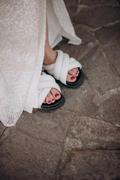 Gelinin bacakları parlak beyaz bir gece elbisesi ve rahat ayakkabılar içinde. Rahat kıyafetler giyin.
