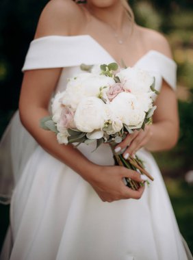 Gelin, beyaz şakayık, güller, okaliptüs buketini yakından çek. Gelin elinde beyaz, zarif, saten bir elbiseyle bir buket tutuyor.