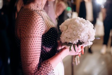 Gelinin beyaz ortanca buketine yakın çekim. Gelinin çekici bir gece elbisesi içindeki arkadaşı gelinin buketini yakaladı. Kızın yarım bir sırası var.