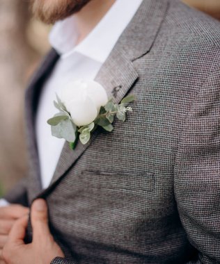 Damadın ceketinin yakasında solmuş yapraklar olan beyaz çiçekli yaka çiçeği.