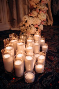 Mavi akşam ışığında yapılan bir düğün töreninde büyük, beyaz, volkanik mumlar yerde duruyor. Sıcak mum ışığı. Sıcak ışık, soğuk gölgeler. Parlak cam. Mumlar yerdeki zarif cam vazolarda yakılır. Düğün için süslemeler.