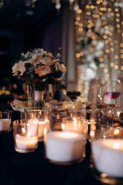 Mavi akşam ışığında yapılan bir düğün töreninde büyük, beyaz, volkanik mumlar yerde duruyor. Sıcak mum ışığı. Sıcak ışık, soğuk gölgeler. Parlak cam. Mumlar yerdeki zarif cam vazolarda yakılır. Düğün için süslemeler.