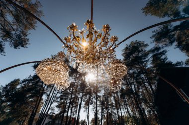 Şatafatlı kristal avizeler gün batımının ışıltısında bir çam ormanının ortasında. Avizeli muhteşem düğün dekoru..