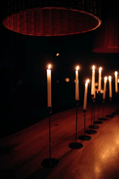 Several tall candles were lit in the dark church. Banquet, restaurant. Table setting. Many tall candles in a dark room, white and tall standing candles with flames