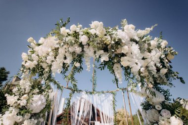 Açık havada düğün töreni. Çimlerde çeşitli taze beyaz çiçeklerle süslenmiş büyük, modern bir düğün kemeri.
