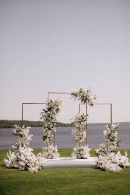 Açık havada düğün töreni. Çimlerde çeşitli taze beyaz çiçeklerle süslenmiş büyük, modern bir düğün kemeri.