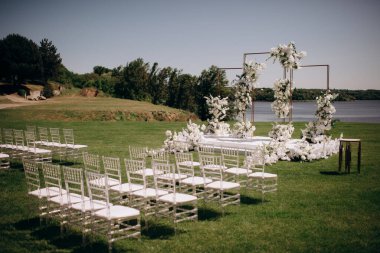Yeşil çimenlikteki bir düğün töreninin süslemeleri. Görkemli büyük ve şık kemer ve chiavari sandalyeler