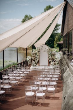 Chiavari sandalyeleri. Açık havada düğün töreni. Bahçede duran şeffaf sandalyeli çeşitli taze beyaz çiçeklerle süslenmiş güzel ve şık bir düğün kemeri. Kutlama günü, konuklar için şeffaf sandalyeler