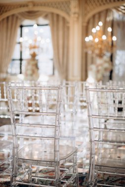 Chiavari sandalyeleri. Açık havada düğün töreni. Bahçede duran şeffaf sandalyeli çeşitli taze beyaz çiçeklerle süslenmiş güzel ve şık bir düğün kemeri. Kutlama günü, konuklar için şeffaf sandalyeler