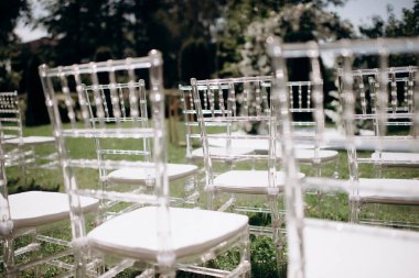 Chiavari sandalyeleri. Açık havada düğün töreni. Bahçede duran şeffaf sandalyeli çeşitli taze beyaz çiçeklerle süslenmiş güzel ve şık bir düğün kemeri. Kutlama günü, konuklar için şeffaf sandalyeler