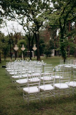 Chiavari sandalyeleri. Açık havada düğün töreni. Bahçede duran şeffaf sandalyeli çeşitli taze beyaz çiçeklerle süslenmiş güzel ve şık bir düğün kemeri. Kutlama günü, konuklar için şeffaf sandalyeler