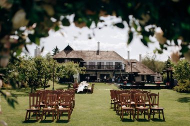 Ahşap sandalyeli düğün koridoru, yeşil bir çayırda doğal, kırsal bir düğün dekoru. Kemer ve ahşap sandalyeli düğün töreni, deniz manzaralı.