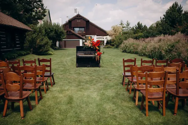 피아노는 결혼식 아치로 오렌지와 빨간색 꽃으로 장식되어 있습니다 의자와 잔디에 스톡 사진
