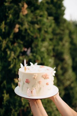 Yuvarlak beyaz pasta, çiçekler, kelebekler ve bir mum.