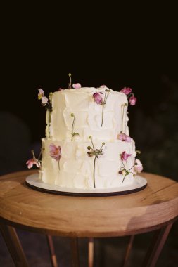 İki katlı beyaz düğün pastası ve ütülenmiş çiçekler.