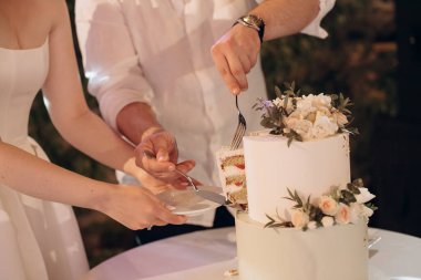 Gelin ve damat iki katlı beyaz bir düğün pastası kesiyor.