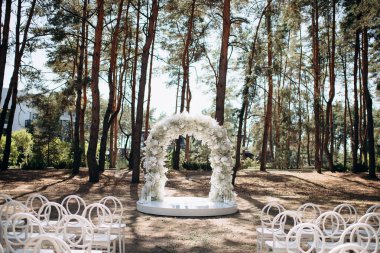 Beyaz narin sandalyeleri ve yumuşak çigila kemeri olan bir çam ormanında güzel bir düğün sahnesi. Doğal ortam huzurlu ve romantik bir atmosfer yaratır.