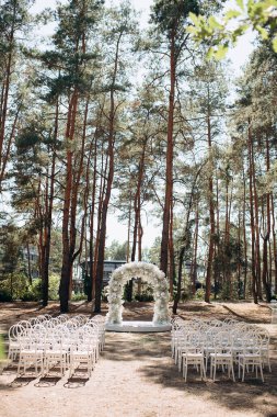 Beyaz narin sandalyeleri ve yumuşak çigila kemeri olan bir çam ormanında güzel bir düğün sahnesi. Doğal ortam huzurlu ve romantik bir atmosfer yaratır.