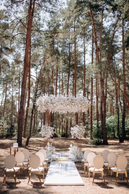 Bir çam ormanında gösterişli bir düğün, beyaz ayaklı zarif beyaz sandalyeler, beyaz çiçeklerle süslenmiş uzun bir kemer ve el değmemiş beyaz bir koridor.