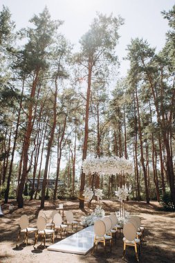 Bir çam ormanında gösterişli bir düğün, beyaz ayaklı zarif beyaz sandalyeler, beyaz çiçeklerle süslenmiş uzun bir kemer ve el değmemiş beyaz bir koridor.
