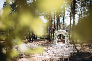 Beyaz narin sandalyeleri ve yumuşak çigila kemeri olan bir çam ormanında güzel bir düğün sahnesi. Doğal ortam huzurlu ve romantik bir atmosfer yaratır.